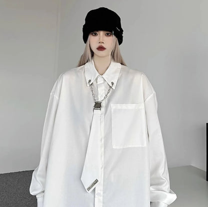 白のオーバーサイズシャツを着用した正面写真。黒いニット帽を合わせ、襟元にはメタルチェーンとクリップの装飾が付いたネクタイ風デザイン。