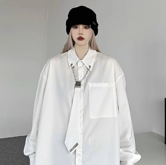 白のオーバーサイズシャツを着用した正面写真。黒いニット帽を合わせ、襟元にはメタルチェーンとクリップの装飾が付いたネクタイ風デザイン。