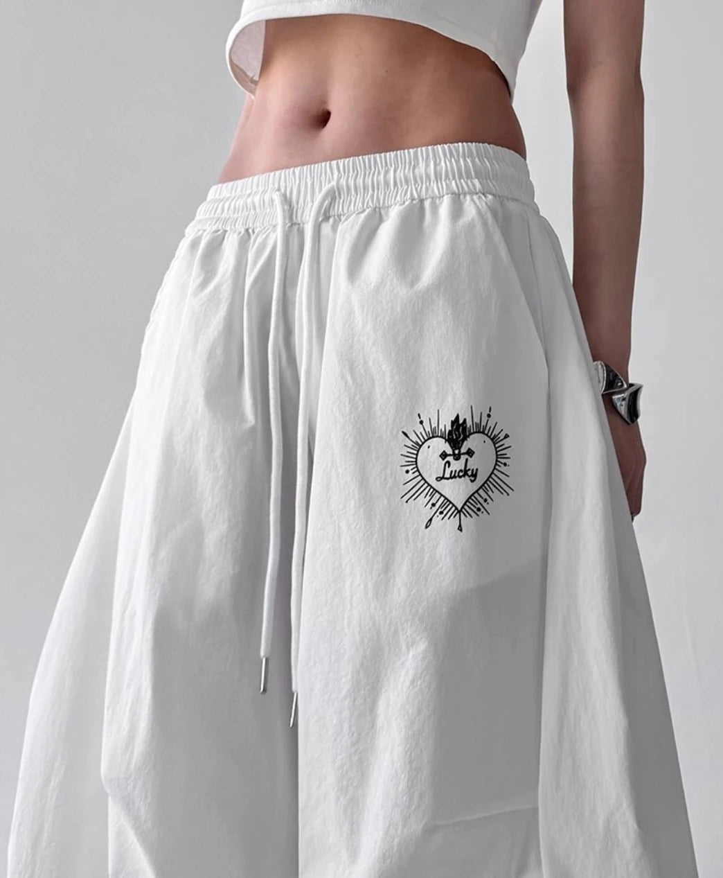 白のパンツのウエスト部分のアップ。ゴムウエスト、ドローコード、そしてハートのデザインのワンポイント刺繍の詳細。