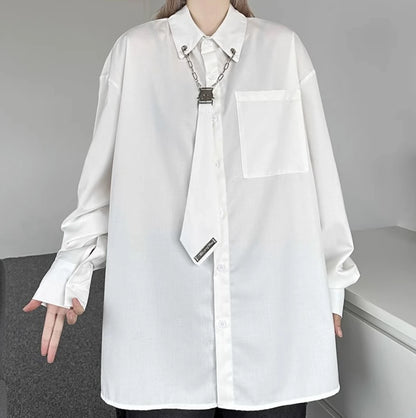 白のオーバーサイズシャツのフロントディテール。首から下のアングルで、襟元のシルバーチェーンとメタルクリップの装飾を強調。