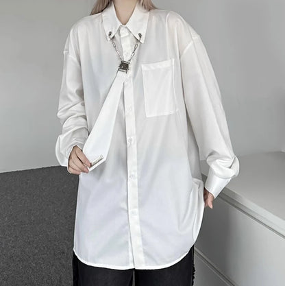 白のオーバーサイズシャツを着用した斜めからのアングル。ゆったりとしたシルエットと、特徴的なメタルチェーンのネクタイデザイン。