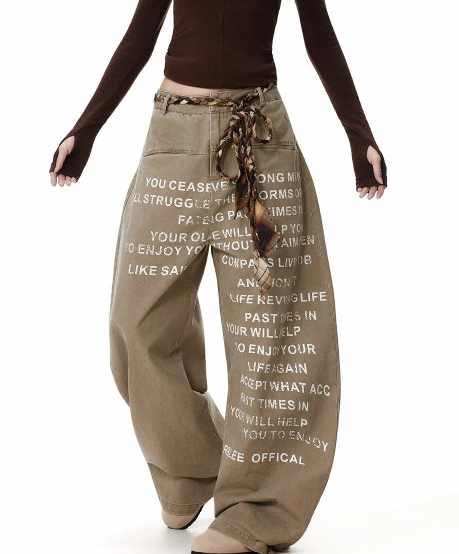 ベージュのワイドレッグトラウザーを着用し、両腕を広げたポーズ。パンツのボリューム感とプリントデザインを強調。